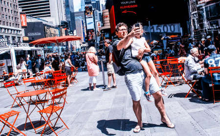 New York, NY/ USA August 9th 2015: A man taking Selfie with daughter at times square Newyork standing near some red chairs and tables.のeditorial素材