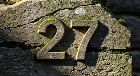 Macro shot of stone carved digits 27 on rough rock surface. Old textured masonry displays numbers...