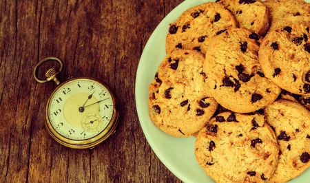 Vintage chocolate cookies with old clock on wood backgroundの写真素材