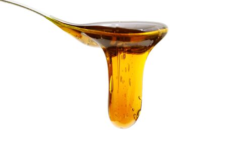 Tiny drops of honey in a wooden spoon over white backgroundの写真素材