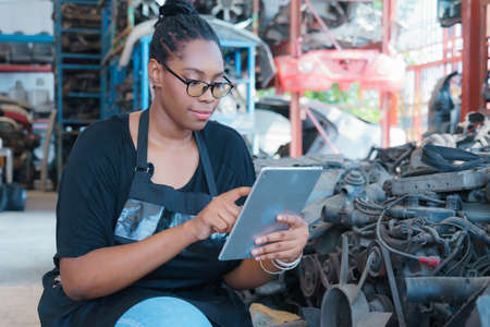 Black African worker woman sitting, checking product and using tablet in factory-warehouseの写真素材