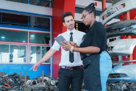Diversity of two people, caucasian business manager point to goods and black African worker woman show detail on a tablet in factory-warehouseの写真素材