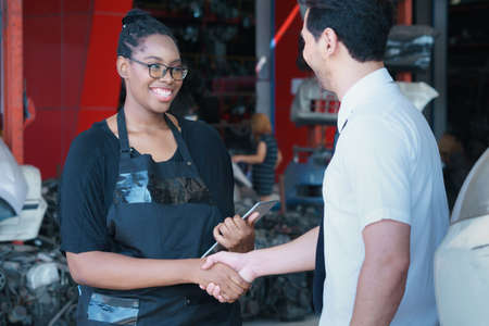 Diversity of two people, caucasian business manager and African worker woman are smiling and shaking hand in factory-warehouseの写真素材
