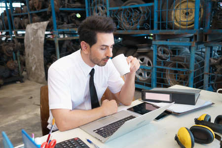 Caucasian business manager sitting at factory-warehouse to analyze online report on laptop-notebook...