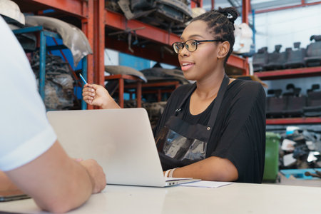 Woman ask man about motor part. Diversity of two people, caucasian business manager work with African worker woman in factory-warehouseの写真素材