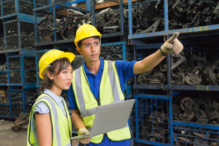 Man and woman work together, diversity of Asian engineer workers stand and man pointing to auto part in factory-warehouseの写真素材