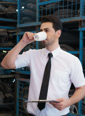 Man drink coffee, holding report. Caucasian business manager drink coffee while holding report in factory-warehouseの写真素材