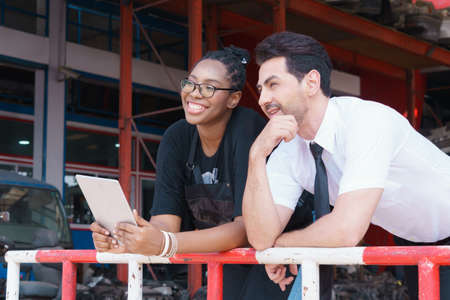 Women and man happy relaxing after working. Diversity of two people, caucasian business manager work with African worker woman in factory-warehouseの写真素材