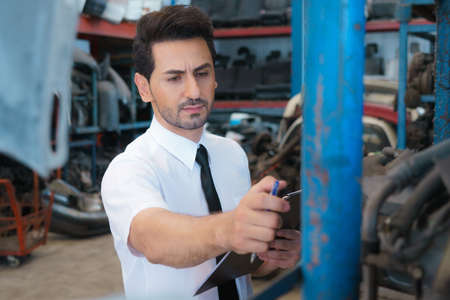 Caucasian business manager stand, checking auto part in factory-warehouseの写真素材