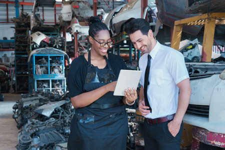 Woman work with man. Diversity of two people, black African worker woman using tablet with caucasian business manager in factory-warehouseの写真素材