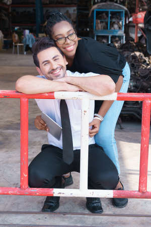 Woman work with man, she hugs and relaxes with him. Diversity of two people, black African worker woman hugs and relaxes with caucasian business manager in factory-warehouseの写真素材