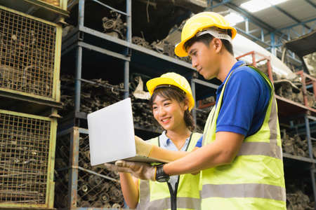 Man and woman work together, diversity of Asian engineer workers stand, laugh and using laptop in factory-warehouseの写真素材