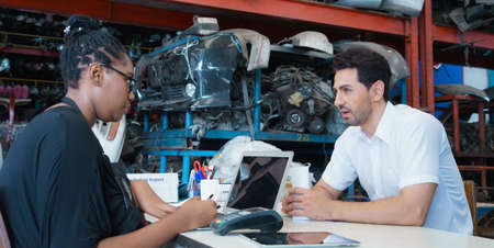 Man work with woman, discuss on serious topic. Diversity of two people, caucasian business manager and black African worker woman serious working in factory-warehouseの写真素材