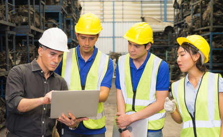Men and woman work together, diversity of Caucasian manager using laptop to explain Asian engineer workers in factory-warehouseの写真素材