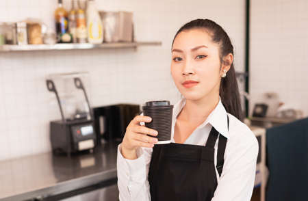 Beautiful Asian barista women show takeaway hot coffee cup at coffee bar in cafe coffee shop....