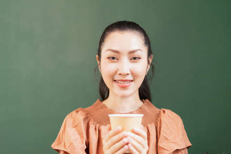 Beautiful Asian woman customer sits and looks straight while holding hot black coffee in takeaway coffee cup in coffee bar. Barista work at coffee bar and food service businessの写真素材