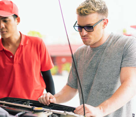 White caucasian car owner looks sad and looking at main auto car engine problem after filling high...