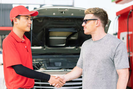 White caucasian car owner and Asian gas station worker man shake hands after succeed maintainance auto car engine and filling high energy power fuel in auto car tank in petrol station, commercial service for benzine, diesel, gasohol, gasoline.の写真素材