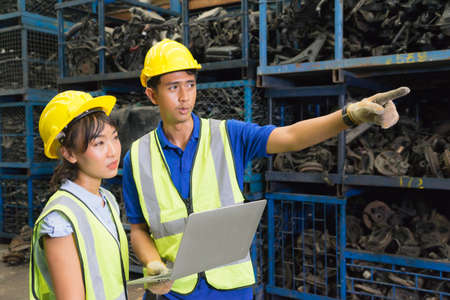 Man and woman work together, Asian engineer worker man point to auto part and Asian engineer woman look at that in factory-warehouseの写真素材