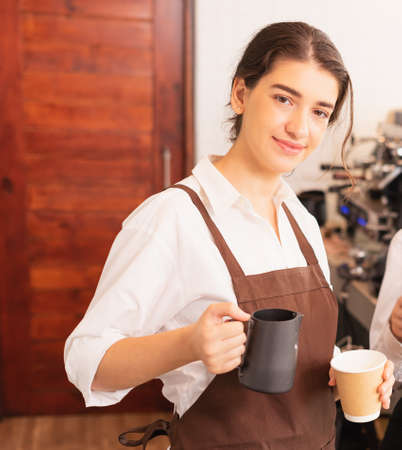 Half-body right side angle of beautiful caucasian barista women fills white milk into takeaway hot...