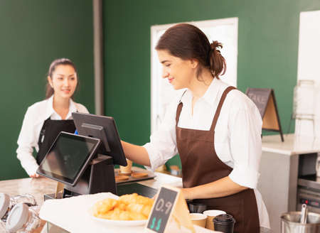 Beautiful caucasian barista woman happy to make online coffee orders on cashier machine at the...