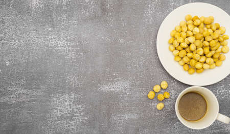 Top view of raw macadamia seeds on plate and coffee cup on stone background, macadamia nuts and coffee cup on right side and copy space at left side of frameの写真素材