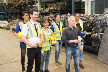Men and woman work together, show teamwork by holding helmets and looking at right side. Caucasian engineer men, black woman, Asian men, Asian woman holding helmets act as smart in factory-warehouseの写真素材