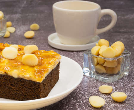 Toffee chocolate cake slice with macadamia seeds in small bowl and coffee cup on stone background for dessert break. Toffee cake made from bake, dark chocolate, macadamia, nut, caramel, and coffeeの写真素材