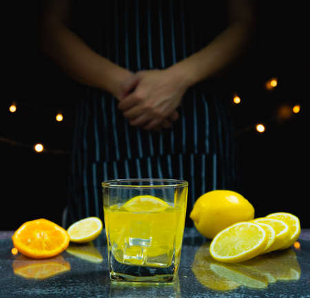 slice fresh lemon, ice in lemon juice glass on table in front of man standing, bartender prepare fruit cocktail or fresh juice for drinking in party at barの写真素材