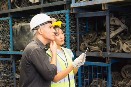 Woman and man work together, diversity of Asian engineer worker woman using tablet and looking to auto part in factory-warehouseの写真素材