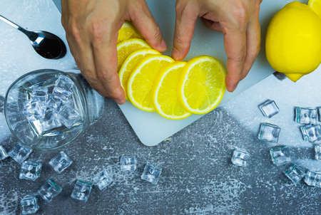 top view of man intend to catch fresh slice lemon on cutting board near lemon, ice, glass on table, bartender prepare fruit cocktail or fresh juice for drinking in party at barの写真素材