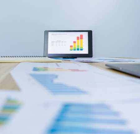 vertical of business data graph on tablet near notebook, document, laptop on working desk, professional worker busy work on the business graph dataの写真素材