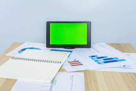 green screen on tablet near notebook, data graph document on working desk for making meeting presentation, professional worker busy work on the business graph dataの写真素材