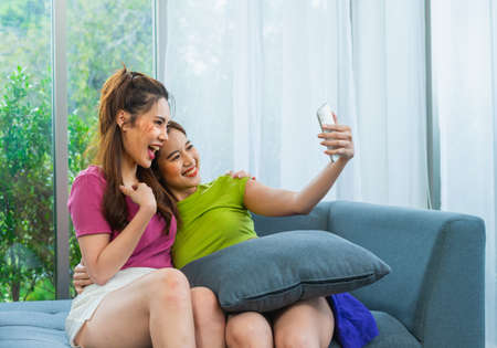 young couple lgbt women happy to live with friend via mobile in living room at home, lifestyle of couple lgbt loving women happy in romance love and funの写真素材