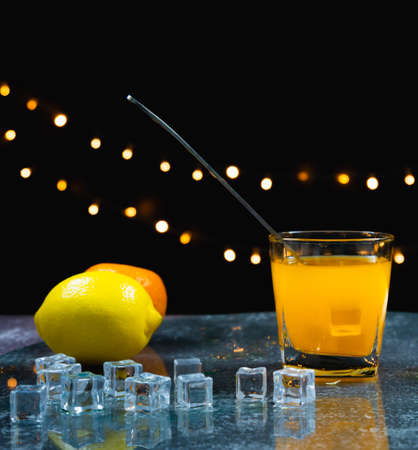 orange juice, ice, spoon in glass near fresh lemon, orange, ice on table, bartender prepare fruit cocktail or fresh juice for drinking in party at barの写真素材