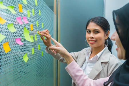 businesswomen happy smile while paste post-it on mirror in office workplace and meeting room,...