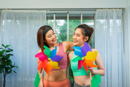 young lgbt women smile together, hold colorful turbine at home, lifestyle of couple lgbt loving women happy and fun in yoga sportsの写真素材