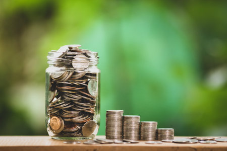 Coins in glass jar with green bokeh background. save money for investment concept.の写真素材