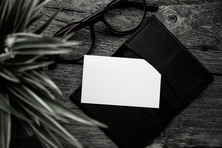 Blank business card with eyeglasses and plant on wooden tableの写真素材