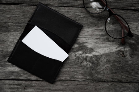 Blank business card with eyeglasses and black wallet on wooden backgroundの写真素材