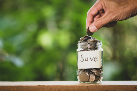 Hand putting coins in the glass jar with save word. Saving money concept.の写真素材
