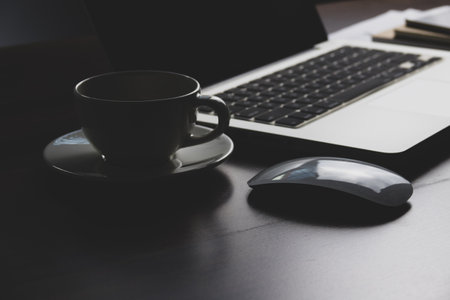Close up of coffee cup with laptop and mouse on wooden table.