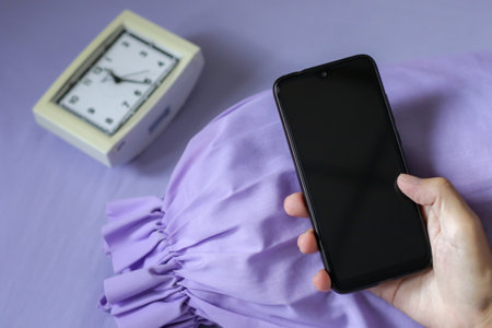 A black smartphone in man hand on purple bed