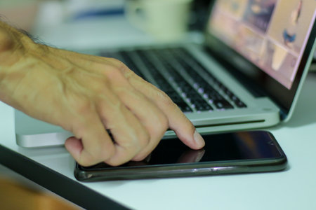 Single finger press on a smartphone with labtop background