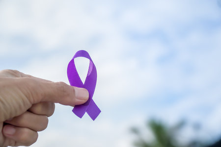 Close-up hand holding breast cancer awareness ribbon with sky and clouds backgroundの写真素材