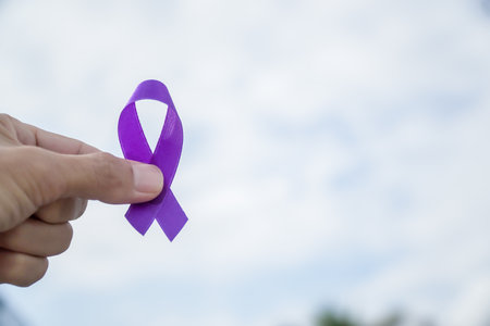 Close-up hand holding breast cancer awareness ribbon with sky and clouds backgroundの写真素材