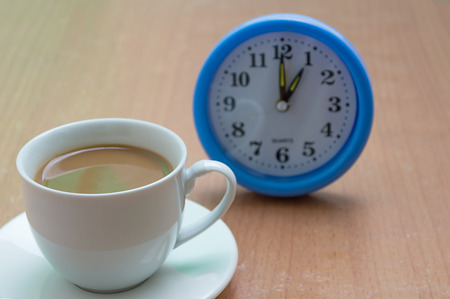 Alarm clock with cup of coffee on wooden backgroundの写真素材
