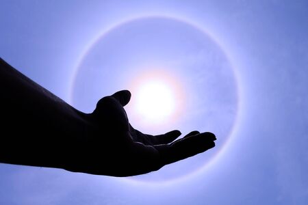 Show hand with sun corona with blue sky background