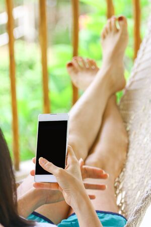 young women using mobile smart phone while relaxing in a cradleの写真素材