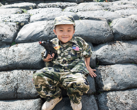 Young boy dressed like a soldier with a gun in barracksの写真素材